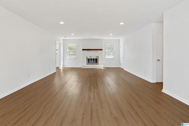 unfurnished living room featuring recessed lighting, a brick fireplace, baseboards, and wood finished floors