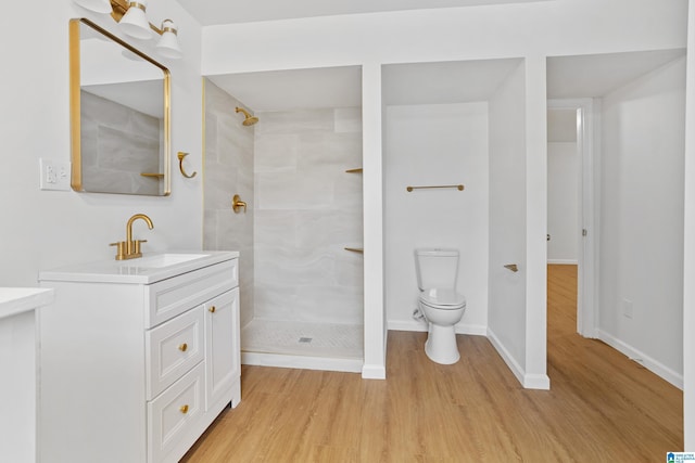 full bath featuring toilet, a tile shower, wood finished floors, and vanity