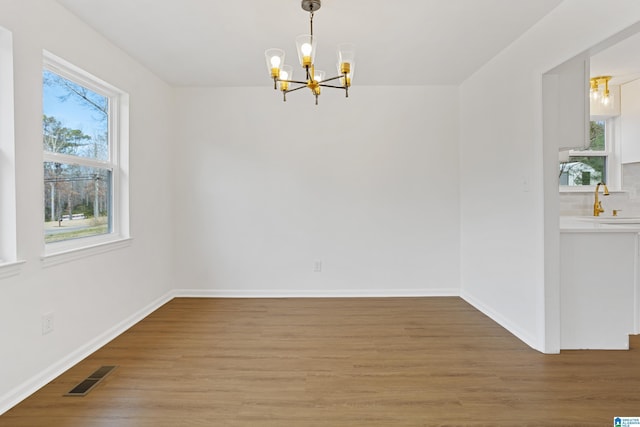 unfurnished dining area featuring light wood-style flooring, a sink, visible vents, baseboards, and an inviting chandelier