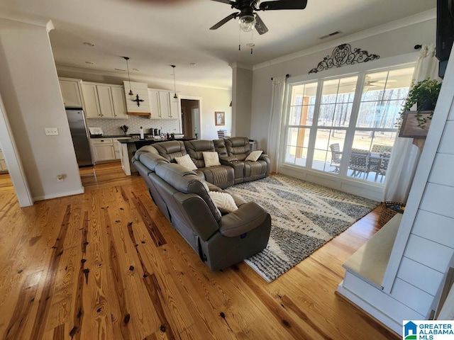 living area with ornamental molding, visible vents, light wood finished floors, and a ceiling fan