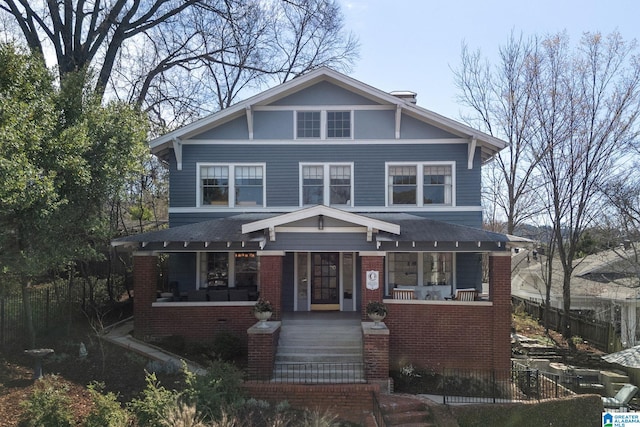 traditional style home featuring brick siding, covered porch, roof with shingles, and fence