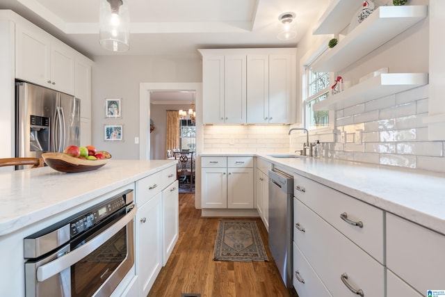 kitchen featuring wood finished floors, a sink, decorative backsplash, white cabinets, and appliances with stainless steel finishes