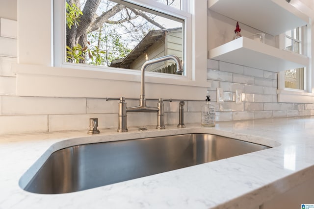 room details with decorative backsplash, open shelves, light stone countertops, and a sink