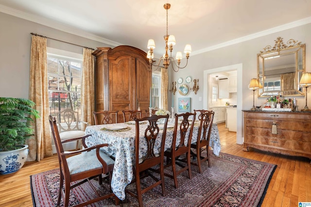 dining area featuring crown molding, light wood-style flooring, and a notable chandelier