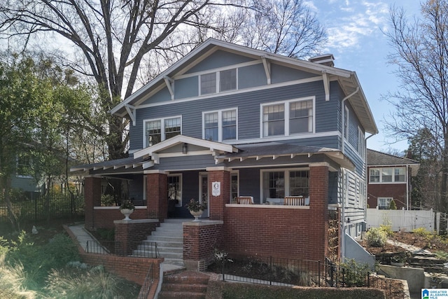 view of front facade with a porch, fence, and brick siding