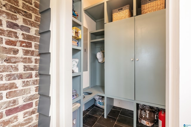 mudroom featuring dark tile patterned floors and brick wall