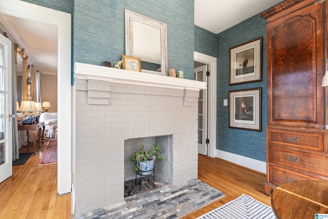 living area with a brick fireplace, wallpapered walls, light wood-type flooring, and baseboards