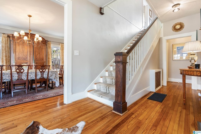 stairs with visible vents, baseboards, ornamental molding, an inviting chandelier, and hardwood / wood-style flooring