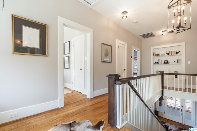 hallway featuring visible vents, an upstairs landing, built in shelves, light wood finished floors, and baseboards