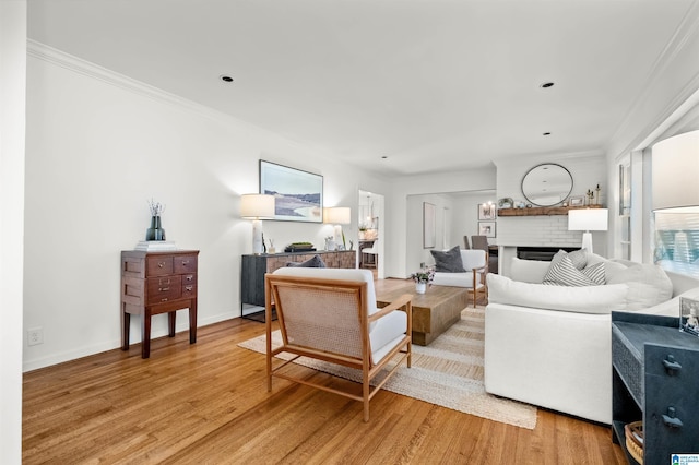 living area featuring light wood finished floors, a fireplace, crown molding, and baseboards