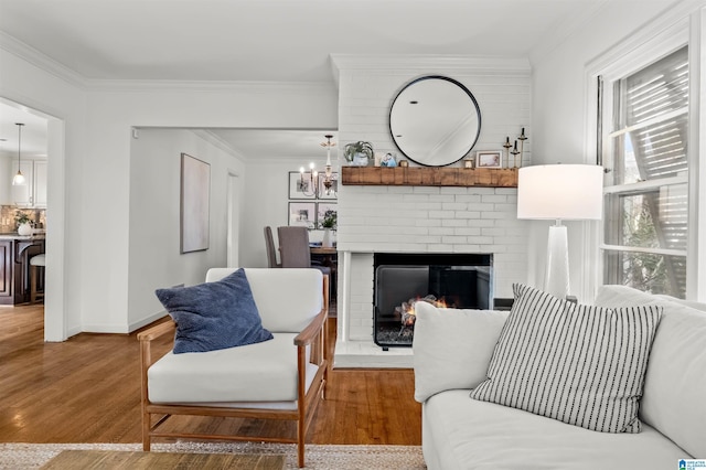 living area featuring baseboards, wood finished floors, a brick fireplace, and ornamental molding