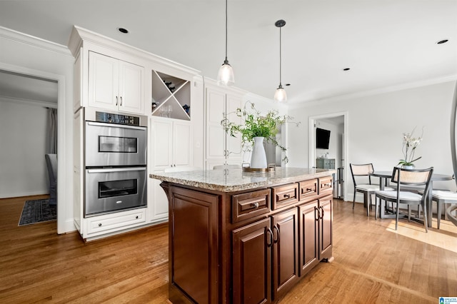 kitchen featuring pendant lighting, ornamental molding, wood finished floors, white cabinetry, and stainless steel double oven