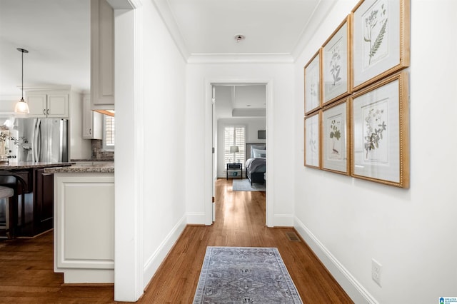 hallway with visible vents, baseboards, dark wood finished floors, and crown molding