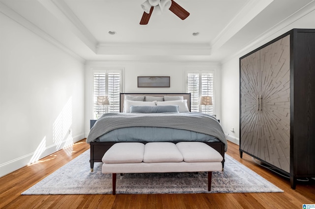 bedroom featuring a tray ceiling, baseboards, and wood finished floors