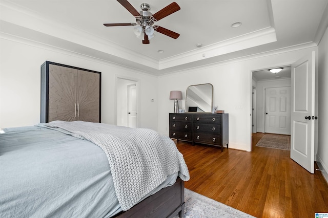 bedroom with a tray ceiling, wood finished floors, a ceiling fan, and ornamental molding