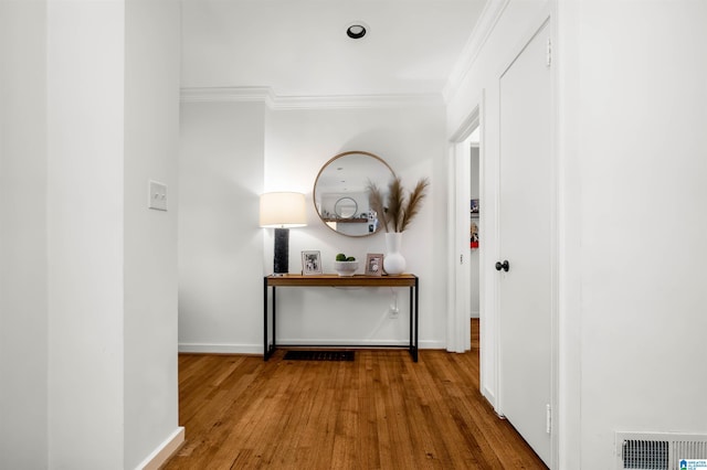 corridor featuring crown molding, wood finished floors, baseboards, and visible vents