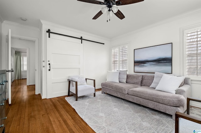 living area featuring crown molding, baseboards, a barn door, wood finished floors, and a ceiling fan