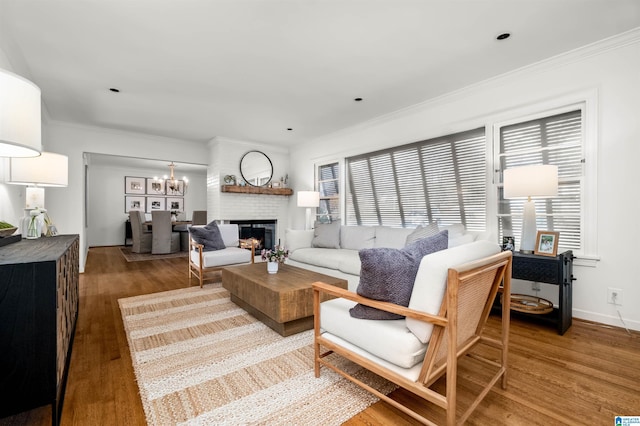 living area featuring ornamental molding, wood finished floors, a fireplace, baseboards, and a chandelier