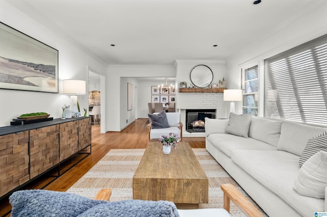 living area with ornamental molding, a fireplace, an inviting chandelier, and wood finished floors