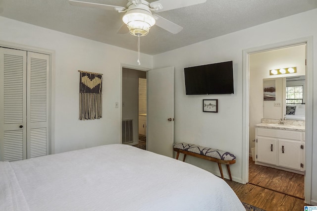 bedroom featuring a closet, visible vents, connected bathroom, wood finished floors, and a sink