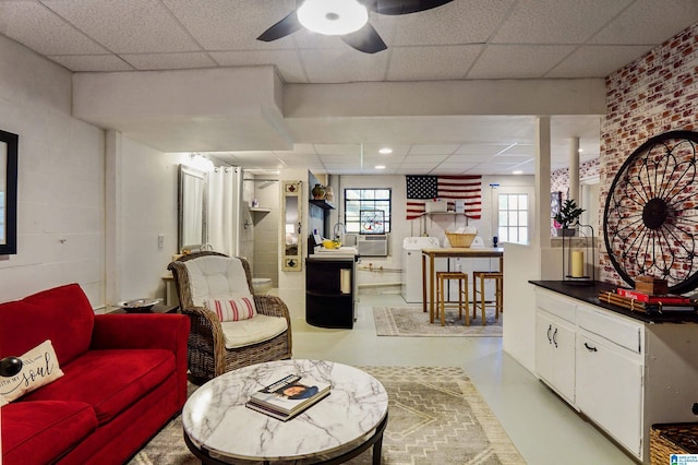 living room featuring concrete flooring, a paneled ceiling, washer / clothes dryer, and a wealth of natural light