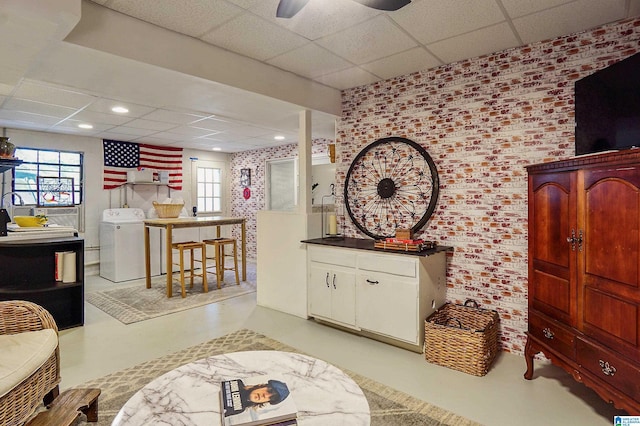 interior space with a paneled ceiling, brick wall, washer / clothes dryer, and concrete flooring