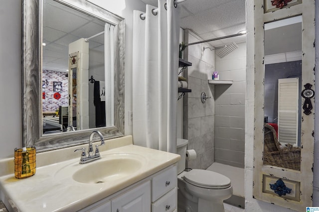 full bathroom featuring a paneled ceiling, tiled shower, vanity, and toilet