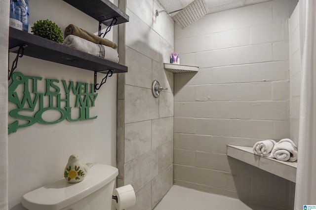 full bath featuring a tile shower, toilet, and concrete block wall