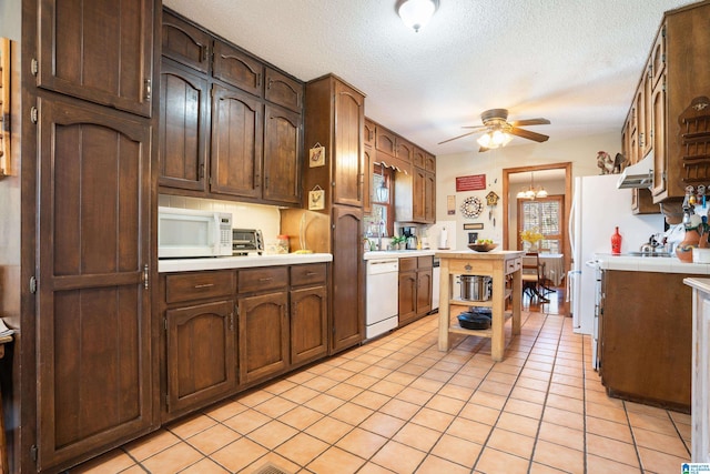 kitchen with a textured ceiling, light tile patterned floors, under cabinet range hood, ceiling fan with notable chandelier, and white appliances