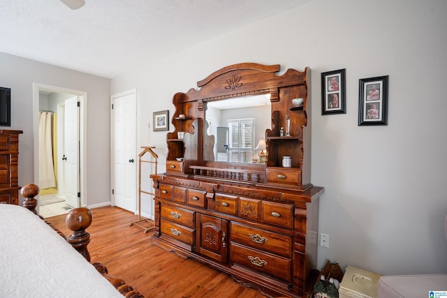 bedroom with baseboards, a textured ceiling, light wood finished floors, and ensuite bathroom