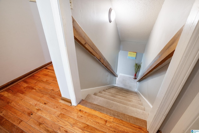 staircase with a textured ceiling, baseboards, and wood finished floors