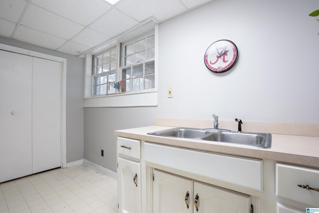 kitchen with a paneled ceiling, baseboards, light countertops, and a sink