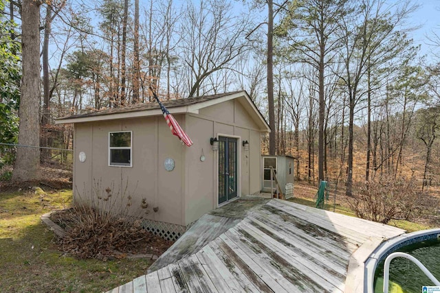 view of front of house with stucco siding, a wooden deck, fence, and an outdoor structure