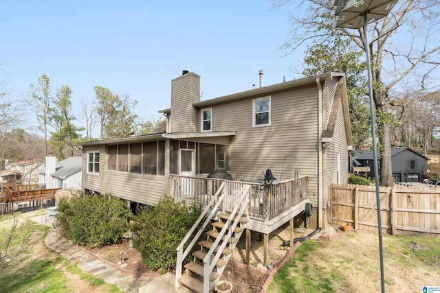 back of house featuring fence, a sunroom, stairs, a wooden deck, and a chimney