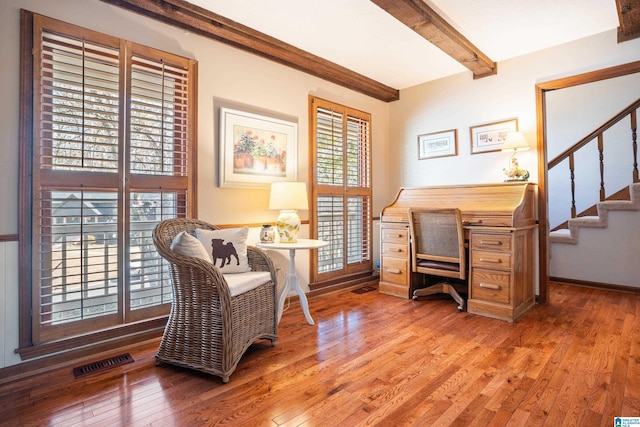 office space with light wood-type flooring, baseboards, visible vents, and beam ceiling