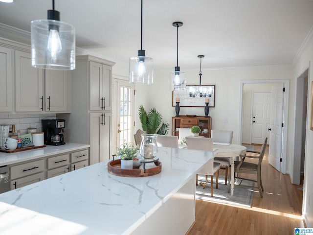 kitchen with light stone counters, light wood-style floors, ornamental molding, tasteful backsplash, and decorative light fixtures