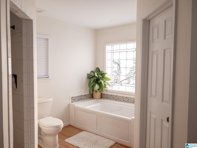 bathroom featuring a garden tub, toilet, and wood finished floors