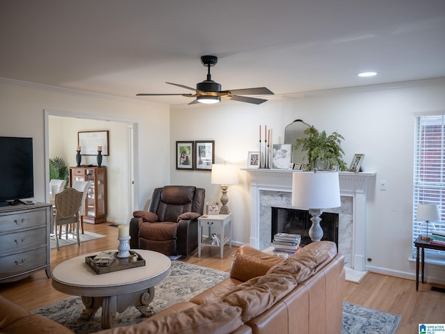 living room featuring baseboards, light wood-style flooring, a premium fireplace, ornamental molding, and ceiling fan