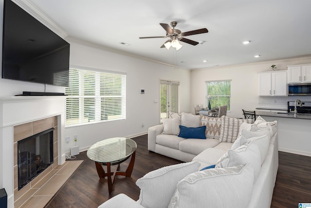 living area with ornamental molding, dark wood finished floors, a fireplace, baseboards, and ceiling fan