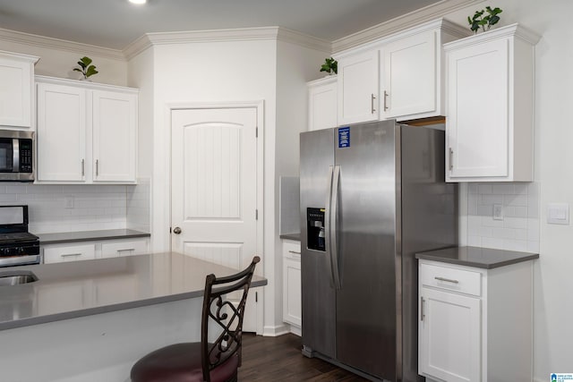 kitchen with ornamental molding, dark wood-type flooring, appliances with stainless steel finishes, white cabinetry, and dark countertops