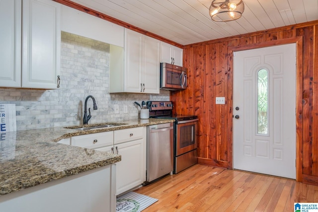 kitchen featuring light stone counters, light wood finished floors, appliances with stainless steel finishes, white cabinets, and a sink