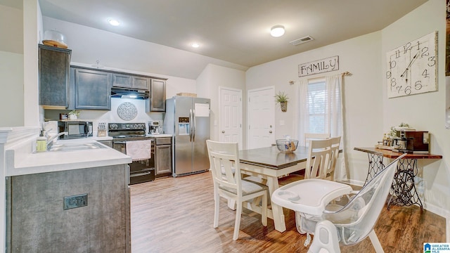 kitchen with range with electric stovetop, light countertops, visible vents, light wood-type flooring, and stainless steel fridge