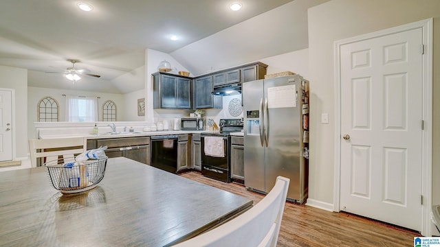 kitchen with lofted ceiling, a sink, wood finished floors, under cabinet range hood, and black appliances