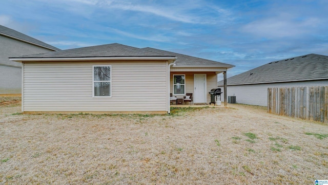 rear view of house with central AC, roof with shingles, and fence