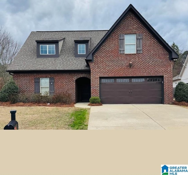 traditional-style home with a front yard, roof with shingles, an attached garage, concrete driveway, and brick siding