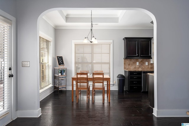 dining space with a raised ceiling, dark wood-style floors, arched walkways, and baseboards