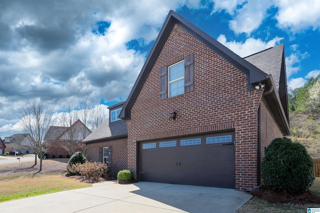 view of side of property featuring driveway, a garage, brick siding, and roof with shingles