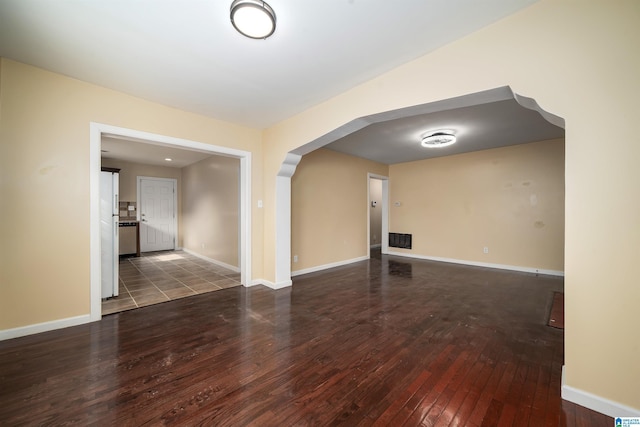 empty room featuring arched walkways, visible vents, baseboards, and wood-type flooring