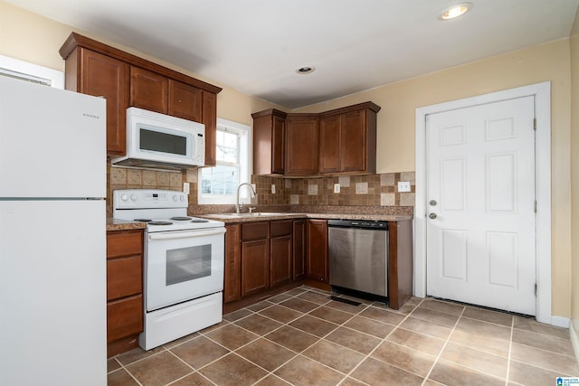 kitchen featuring dark tile patterned floors, decorative backsplash, white appliances, and a sink