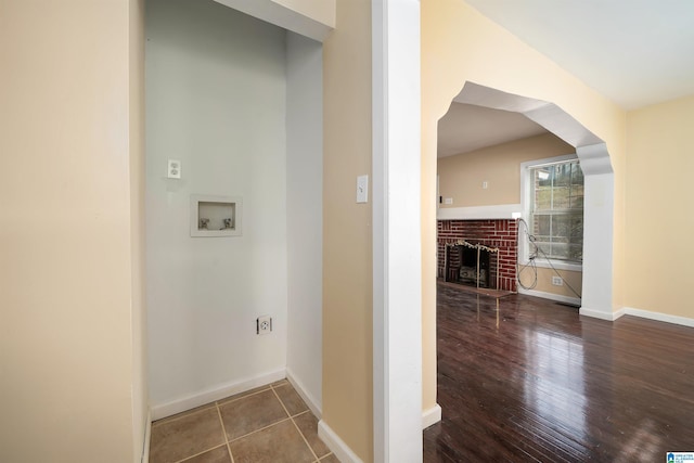 laundry area with washer hookup, a brick fireplace, wood finished floors, and baseboards